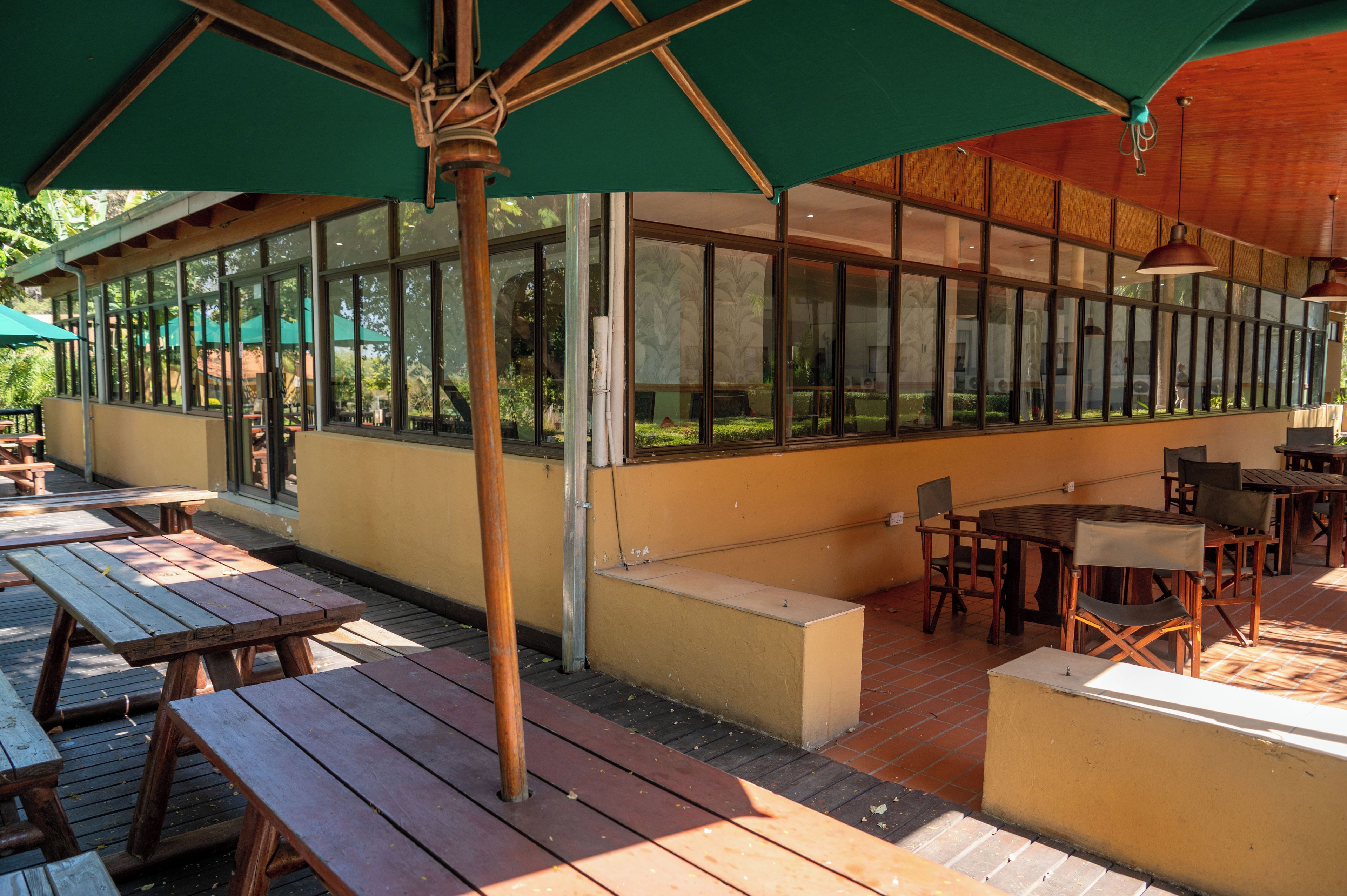 An outdoor patio area with wooden tables and benches, large windows, and a green awning.