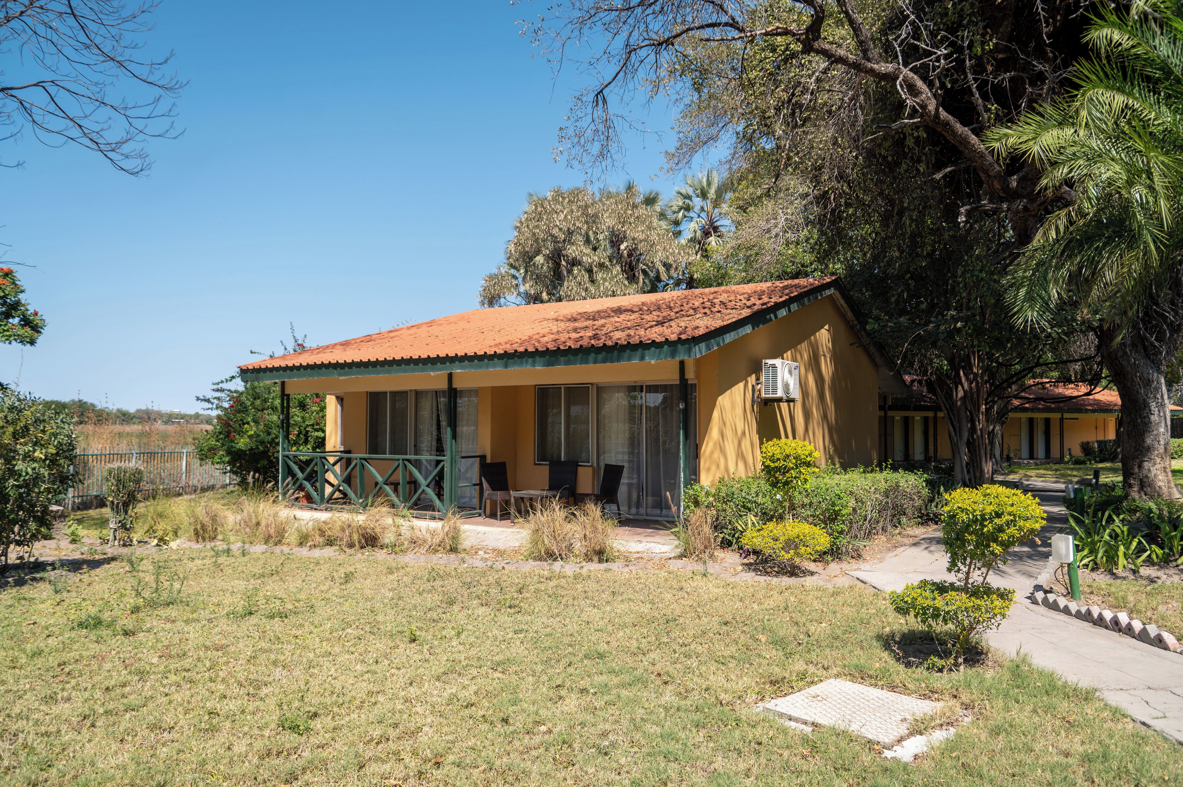 A single-story building with a tiled roof, a covered porch, and a small garden area with various plants.
