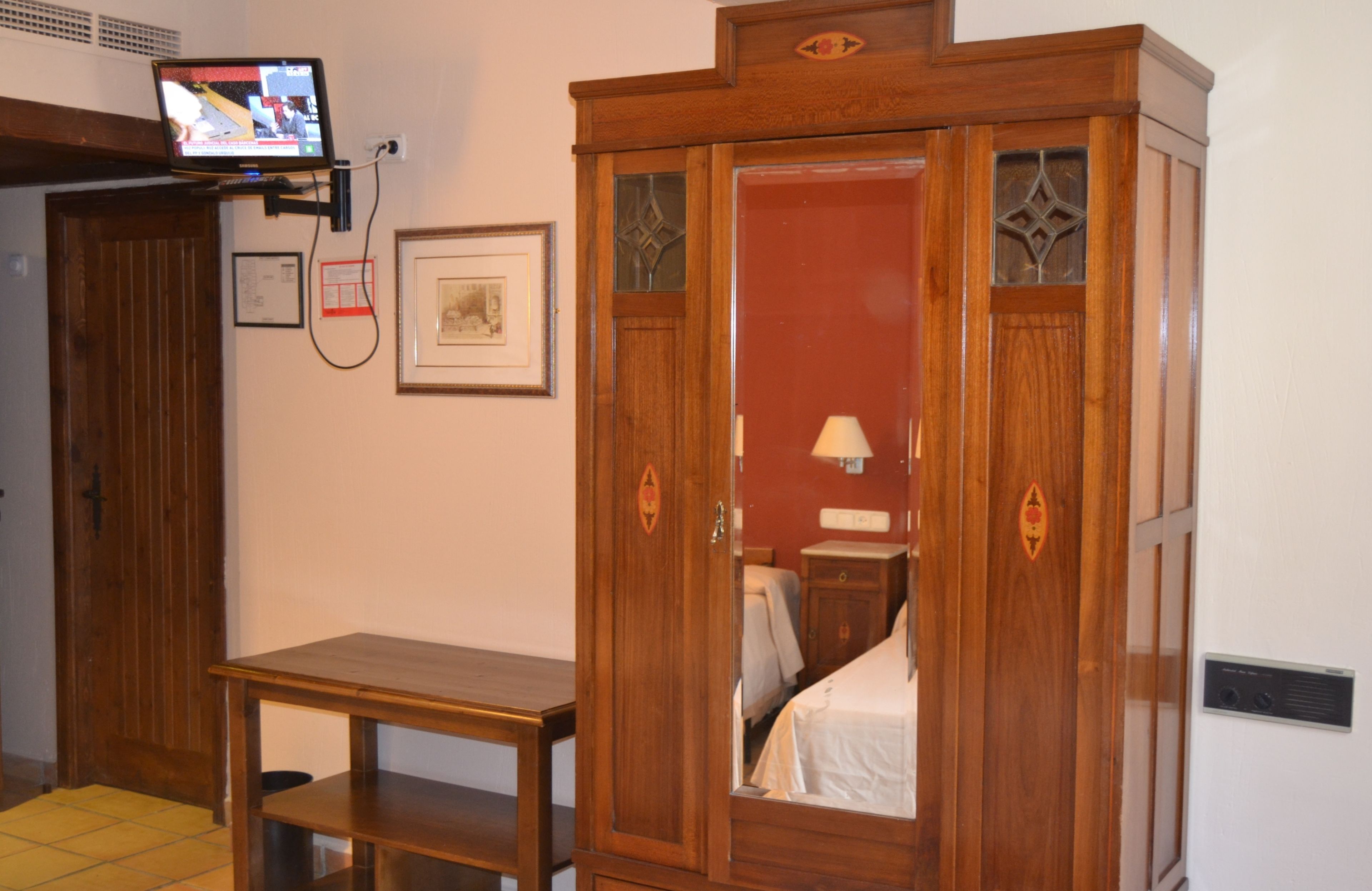 A wooden wardrobe with a mirror, a small table, and a television mounted on the wall.