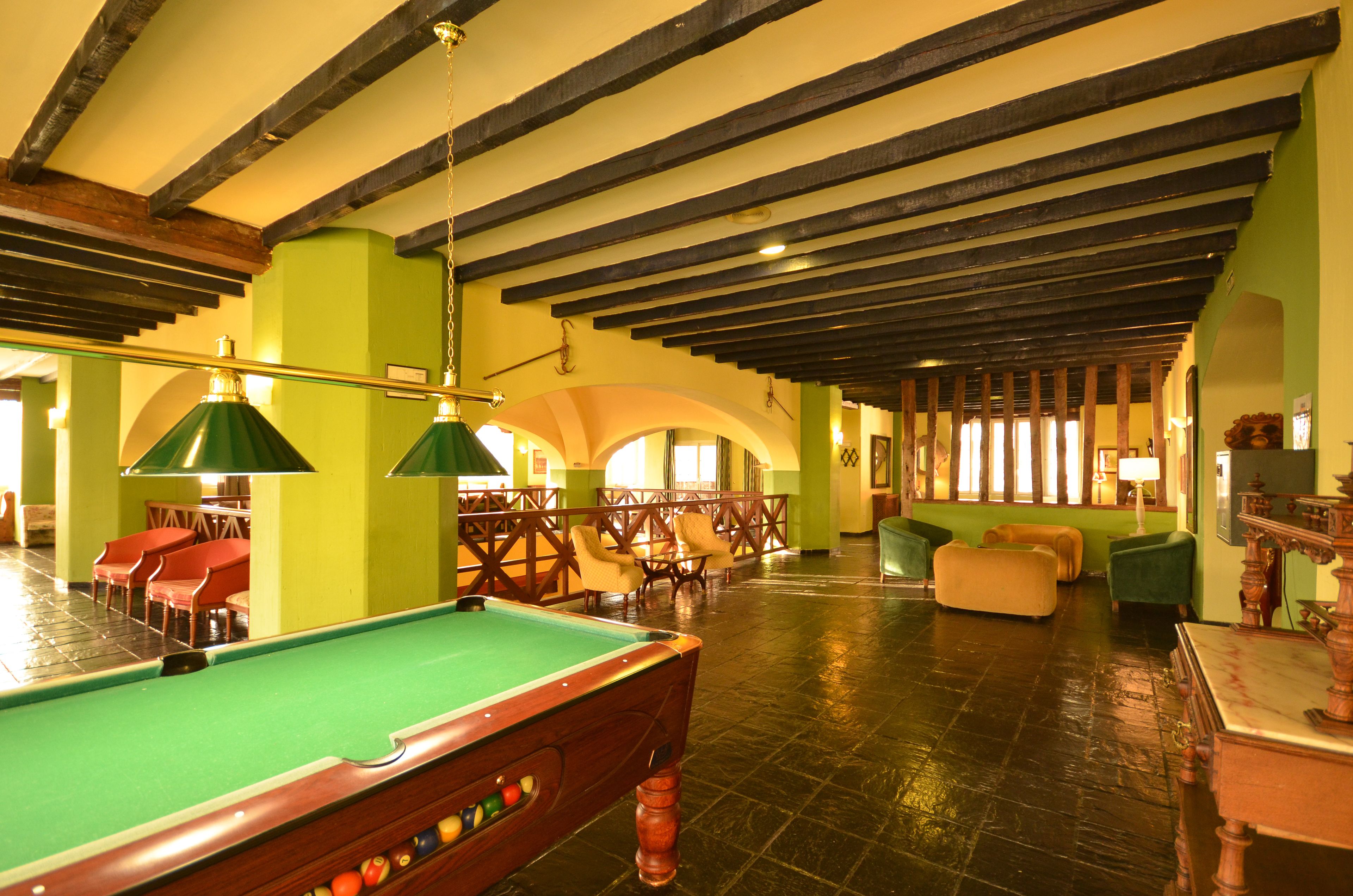 A pool table in a room with wooden beams on the ceiling, green walls, and multiple seating areas.