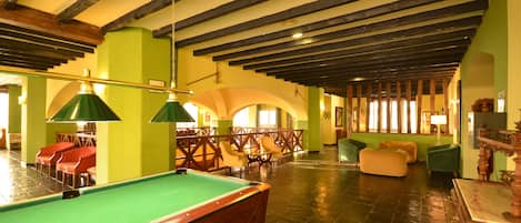 A pool table in a room with wooden beams on the ceiling, green walls, and multiple seating areas.