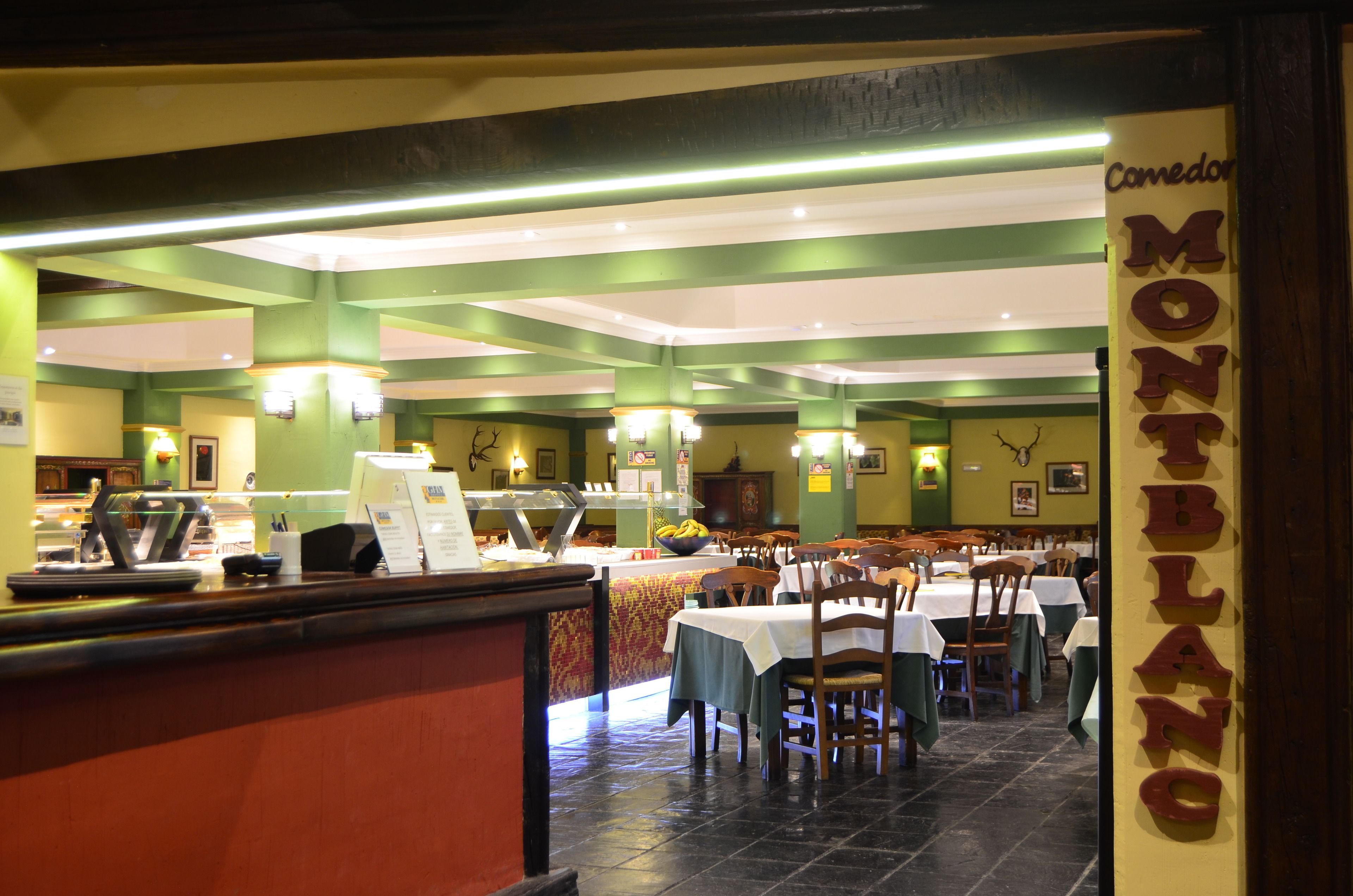 Un restaurant amb decoració verd i blanca, diverses taules i una barra amb un menú.