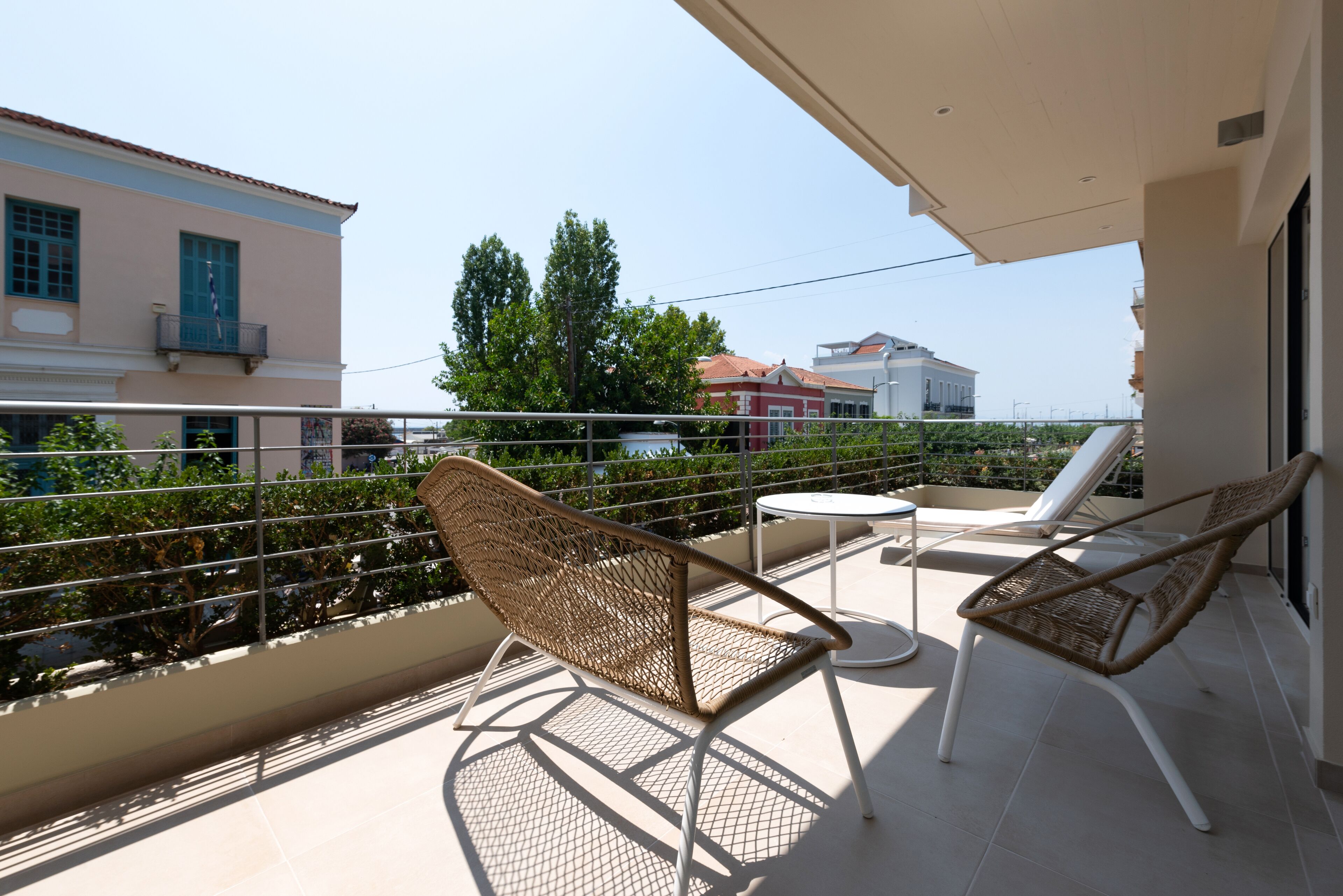 Un balcón con sillas de mimbre y una mesita pequeña, con vista a una zona residencial con casas y árboles.
