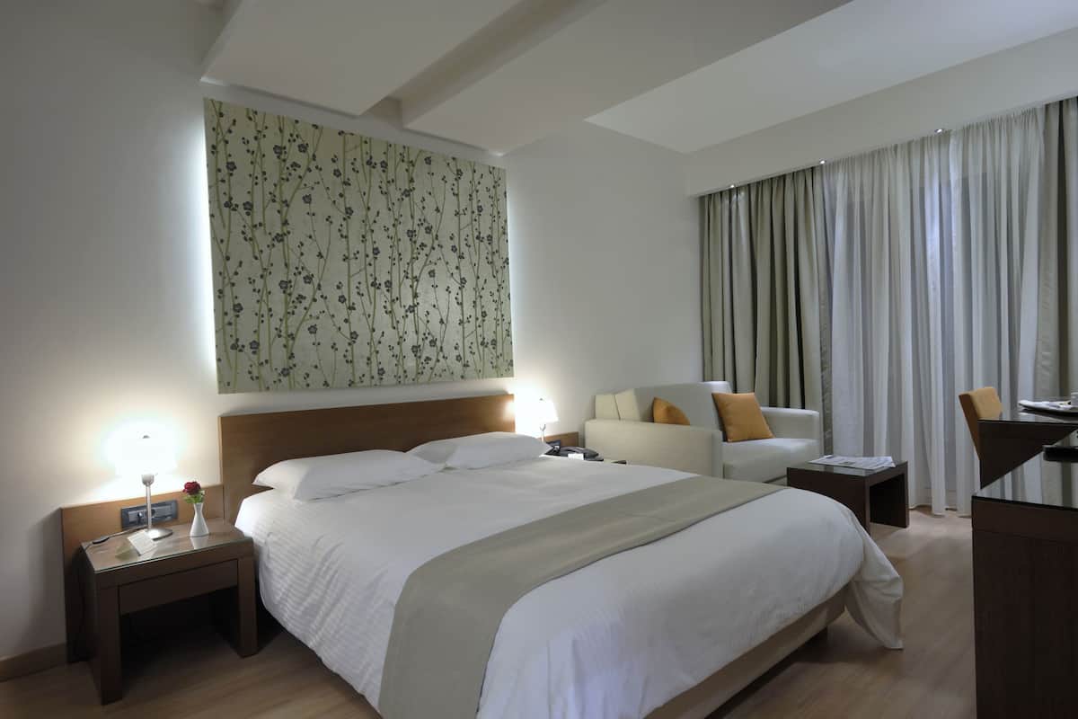 Ein Hotelzimmer mit einem großen Bett, einem Schreibtisch, einem Sessel und einem Nachttisch. Die Wand ist mit einem Blumenmuster versehen.