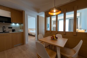 Una cocina moderna con armarios de madera, un microondas negro y un lavamanos. Hay una zona de comedor con una mesa de madera y sillas blancas, y un frutero sobre la mesa.