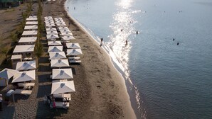 A beach with rows of white umbrellas and lounge chairs, a sandy shore, and people swimming in the water. - Pharae Palace Hotel (Kalamata)