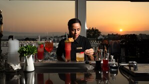 A bar with a bartender preparing drinks, a pitcher of mint, and a sunset view through large windows. - Pharae Palace Hotel (Kalamata)