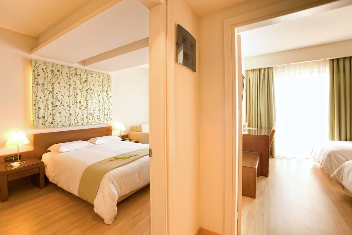 Ein Hotelzimmer mit Bett, Nachttisch, Lampe und einem Spiegel, der das Zimmer reflektiert.