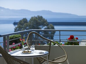 A balcony with a wicker chair and table, a vase with flowers, and a view of a body of water and mountains. - Pharae Palace Hotel (Kalamata)