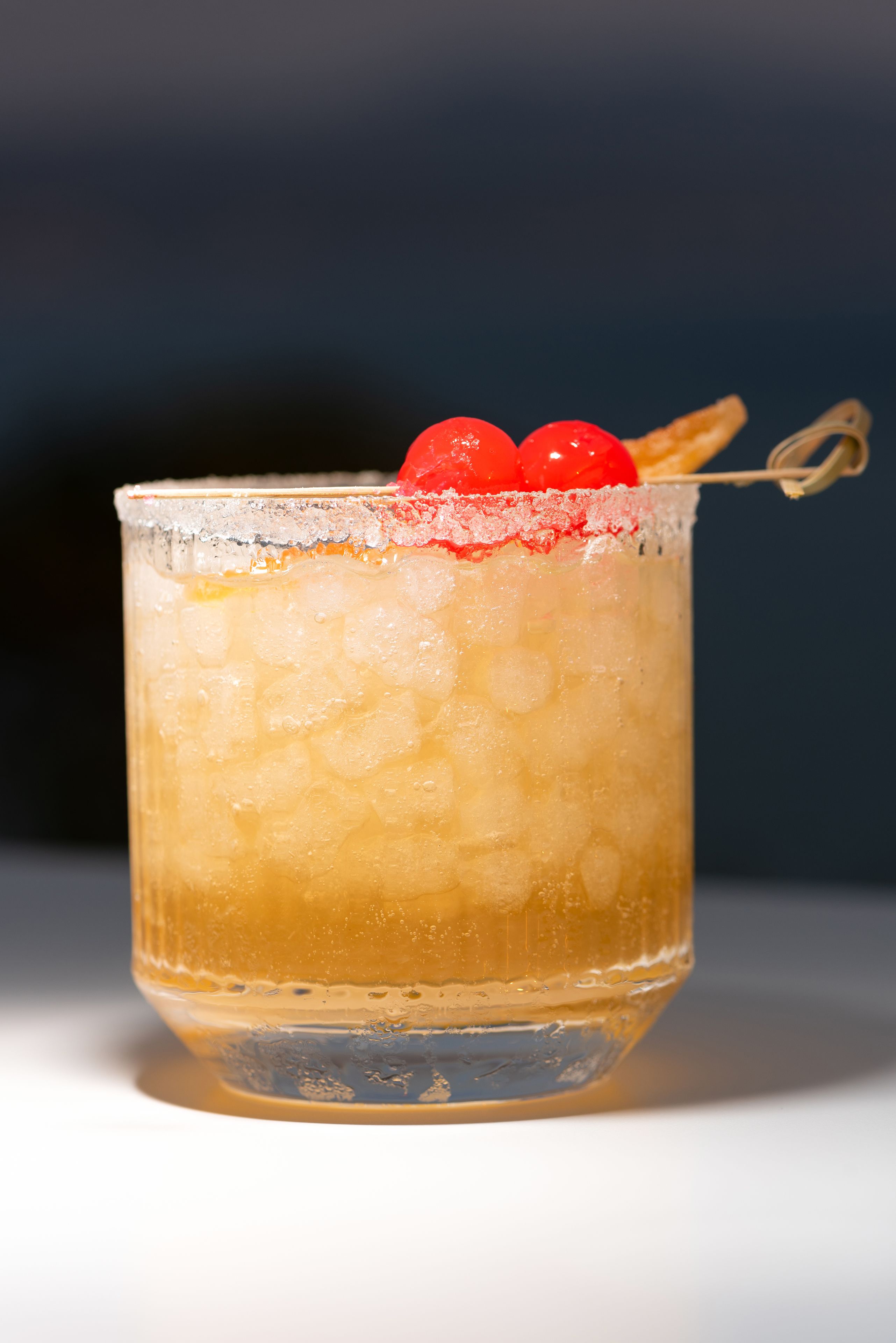 Un verre transparent avec une paille, contenant une boisson rafraîchissante avec des glaçons et une cerise en décoration.