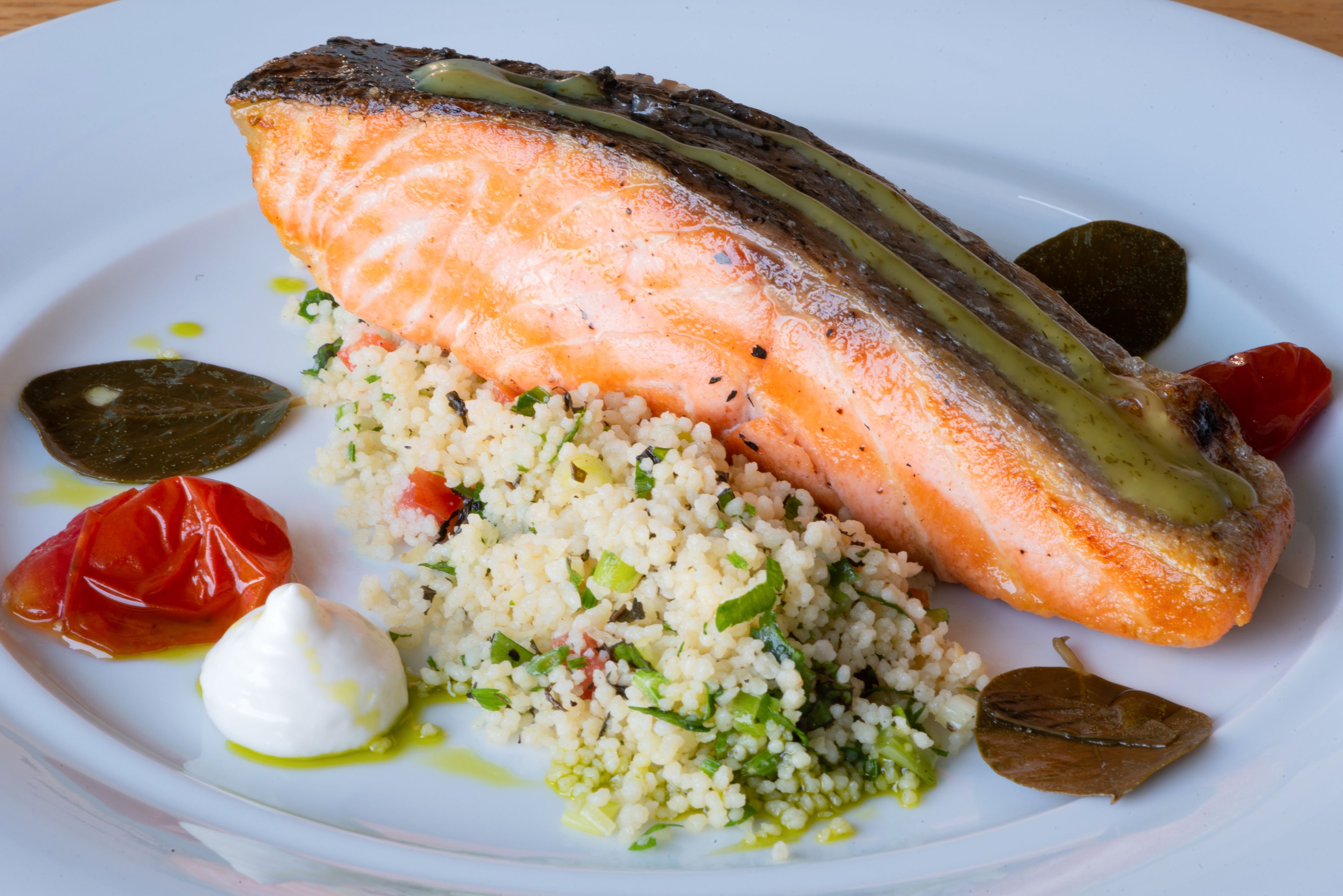 Un plato con salmón, cuscús, tomates cherry y una cucharada de crema.