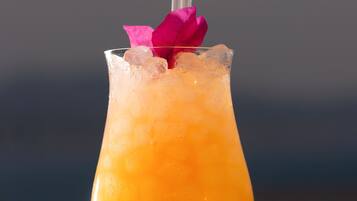A cocktail in a glass with a pink flower garnish and a straw.