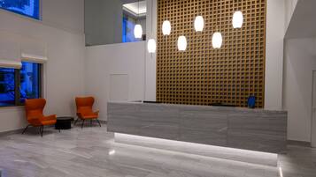 Un área de recepción con mostrador de mármol, dos sillas color naranja, pared de madera con diseño de cuadrícula y un ventanal grande.