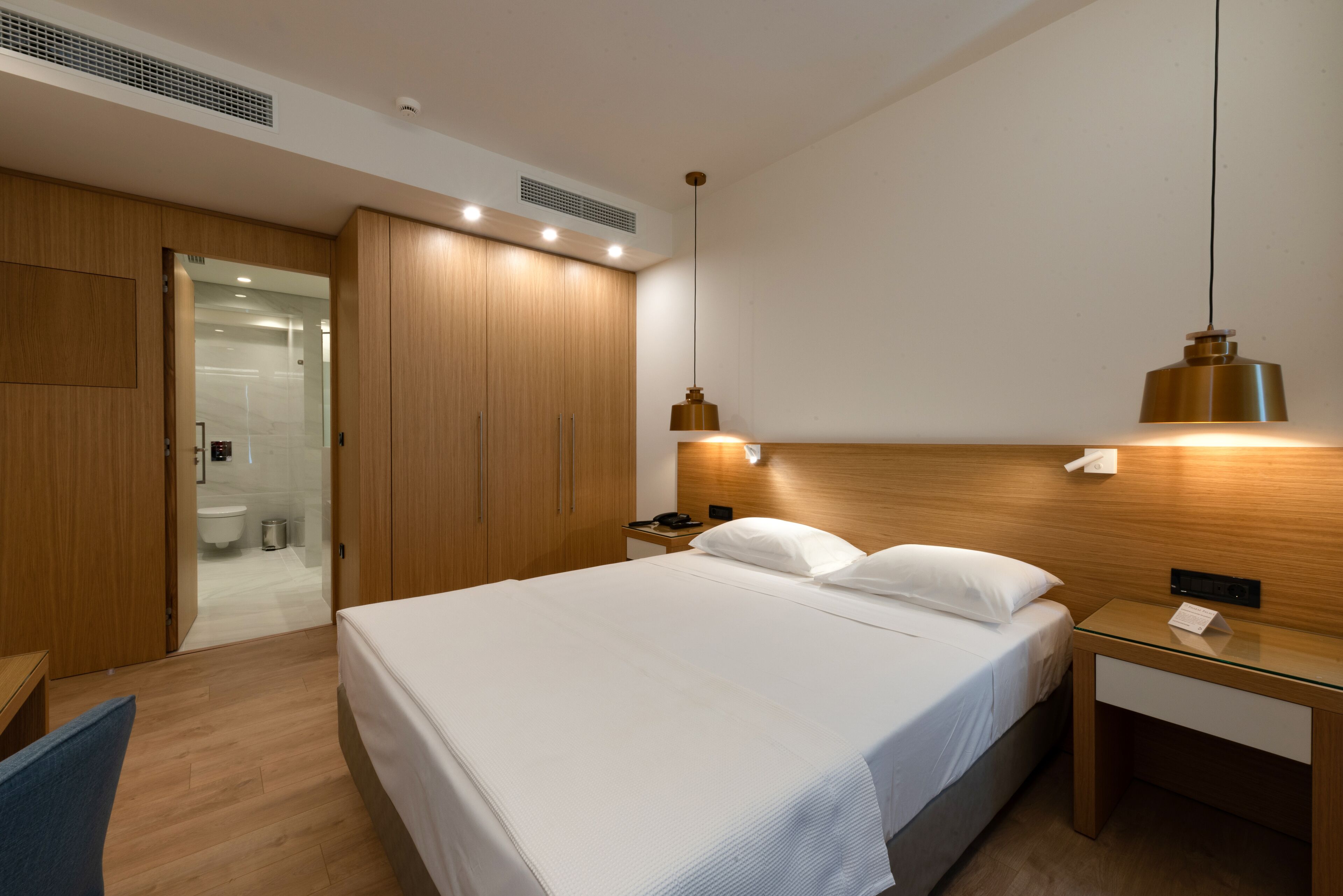 Ett modernt hotellrum med en stor säng, ett träskåp, sängbord och en duschkabin med glasväggar.
