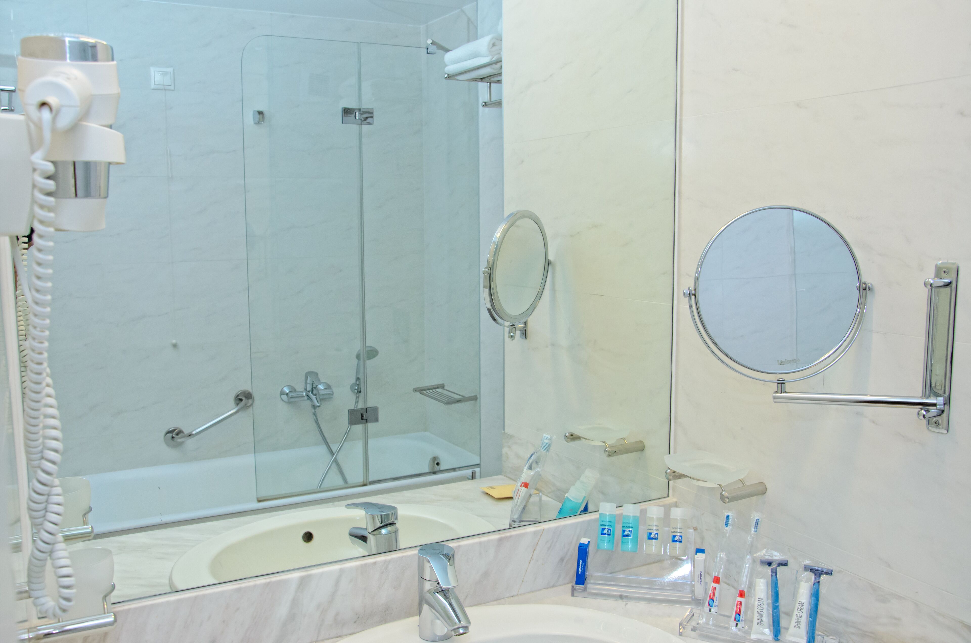 Un baño con un espejo grande, un lavamanos, cabina de ducha con mampara de vidrio y un teléfono.