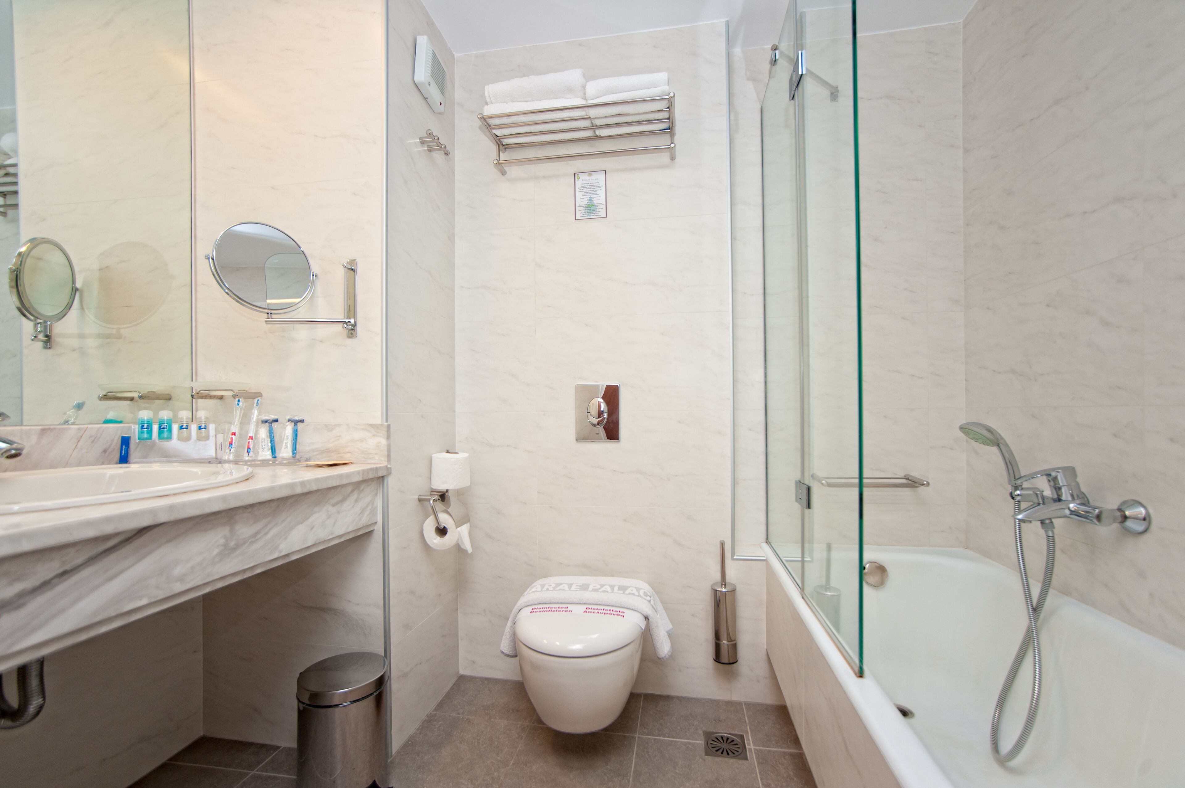 Een moderne badkamer met een marmeren wastafel, een douche met glazen wanden en een toilet met een handdoek erop.