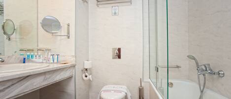 Un baño moderno con lavamanos de mármol, ducha con cerramiento de vidrio y un inodoro con una toalla encima.