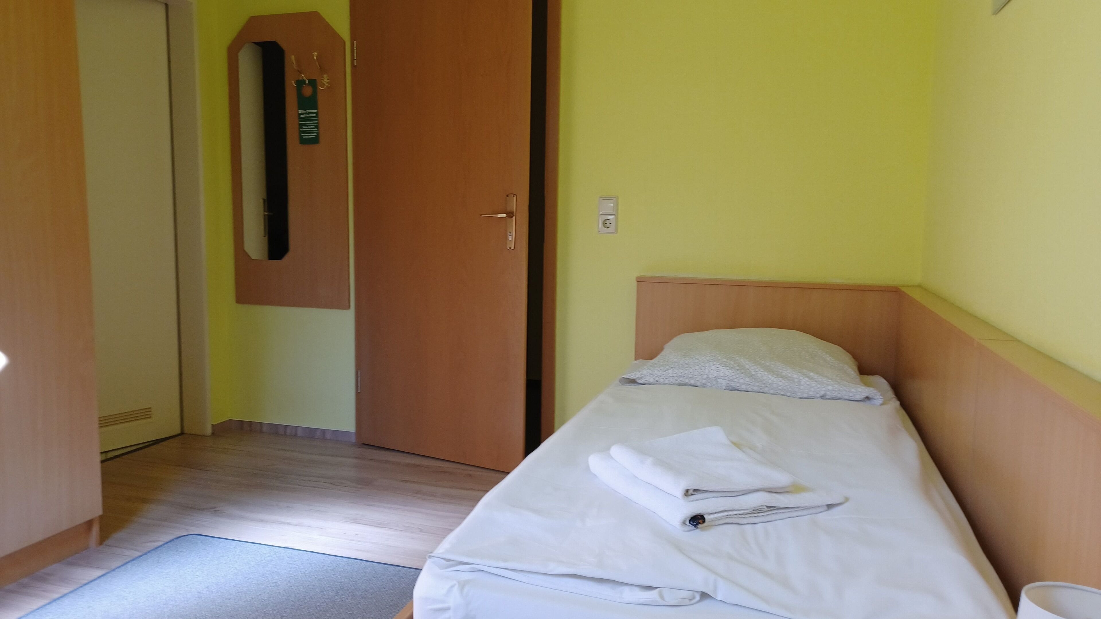 Una cama individual con cabecera de madera, una mesita de noche y un espejo montado en la pared.