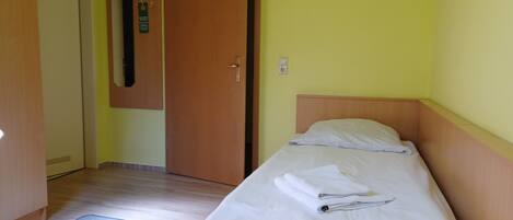 A single bed with a wooden headboard, a bedside table, and a wall-mounted mirror.