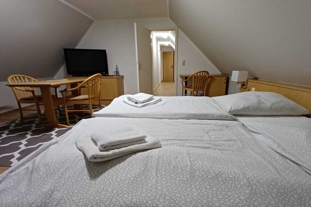 Ein Hotelzimmer mit zwei Betten, einem Schreibtisch, einem Stuhl, einem Fernseher und einem Badezimmer im Hintergrund.