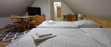 A hotel room with two beds, a desk, a chair, a television, and a bathroom visible in the background.