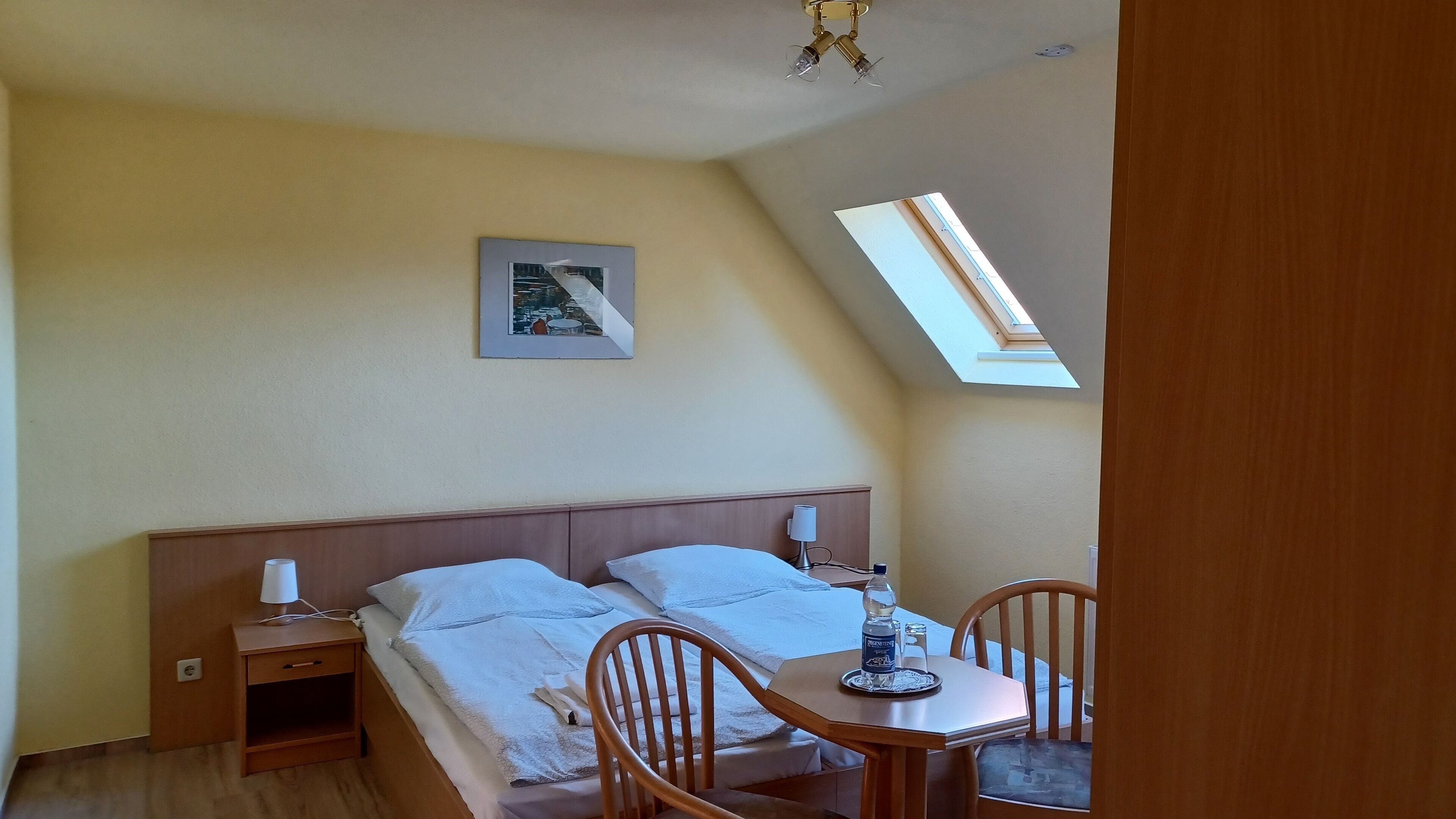 Een slaapkamer met een bed, nachtkastjes, een bureau en een stoel. Boven het bureau bevindt zich een dakraam.