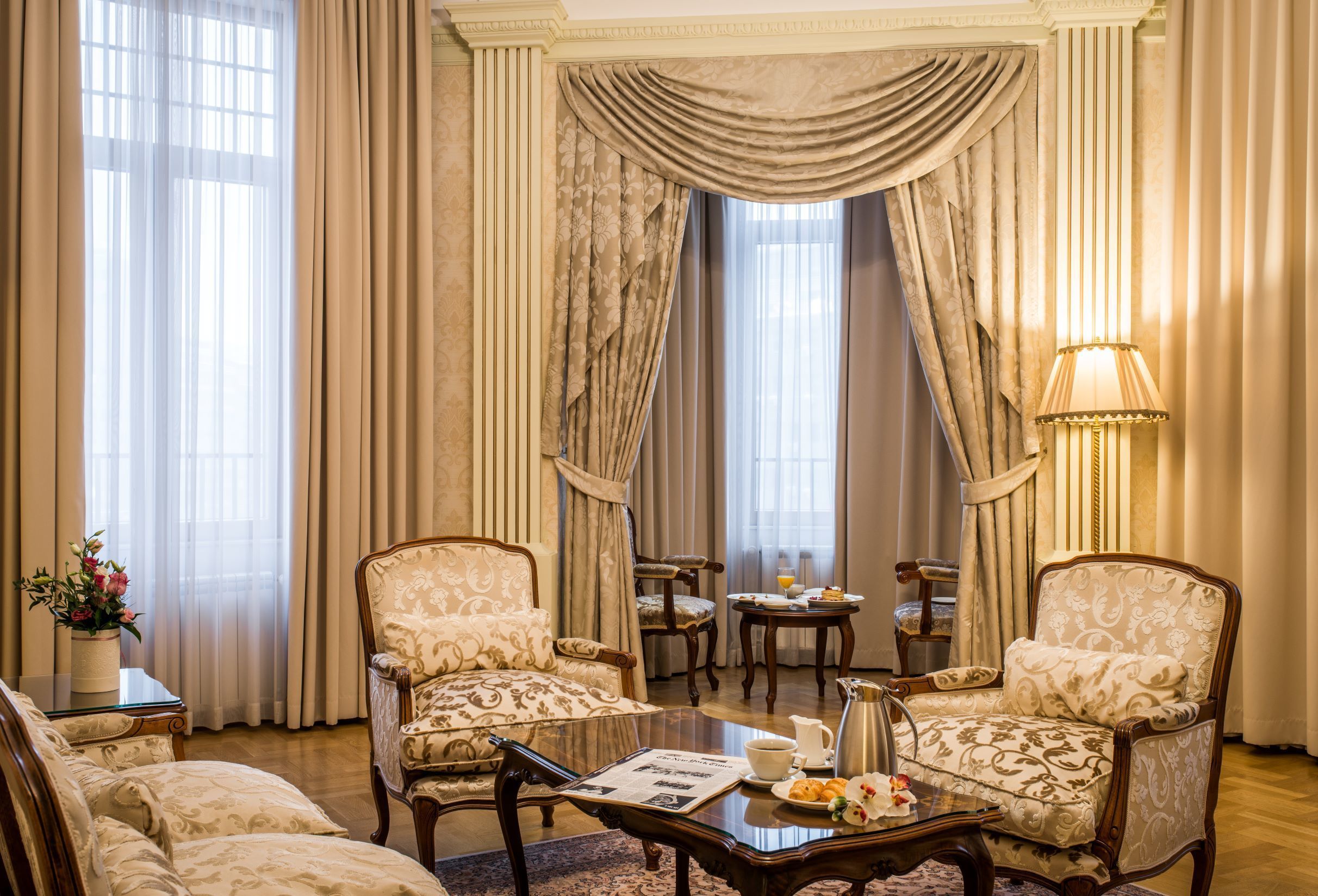 A room with two patterned armchairs, a coffee table, a small table with a pitcher and cups, and a lamp.
