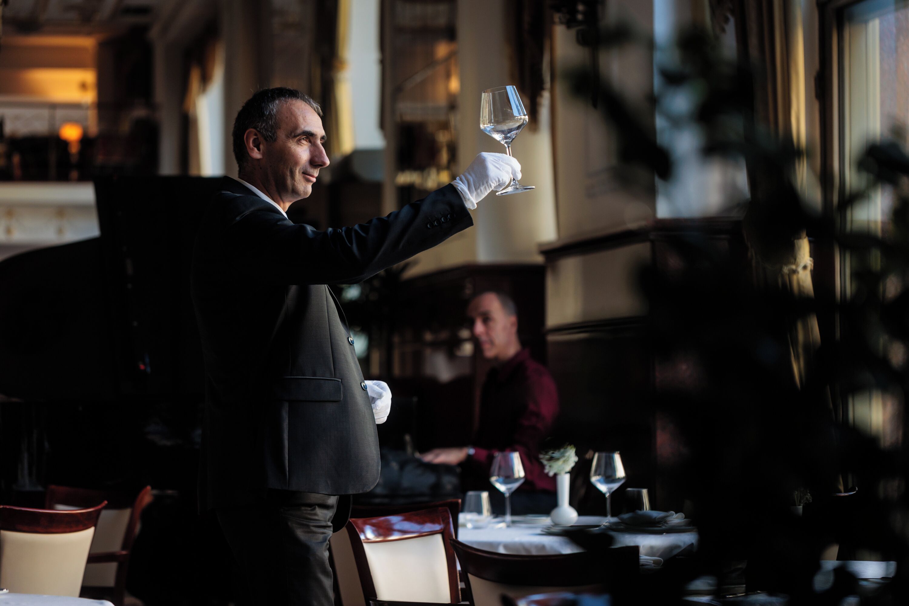 Ein Kellner hält ein Weinglas in einem schummrigen Restaurant mit Tischen und Stühlen.
