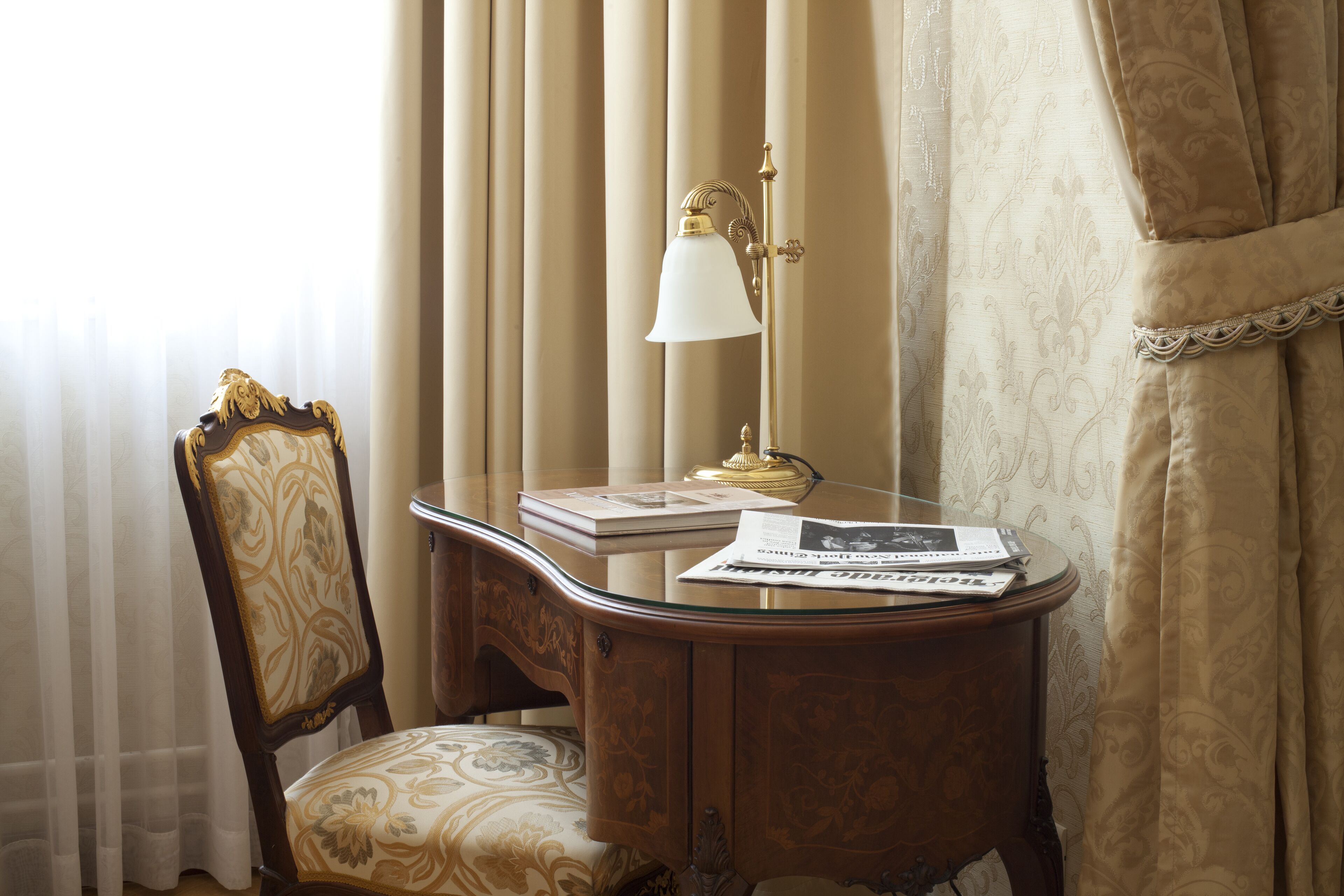 Una habitación con escritorio de madera, una silla, una lámpara y una ventana con cortinas.