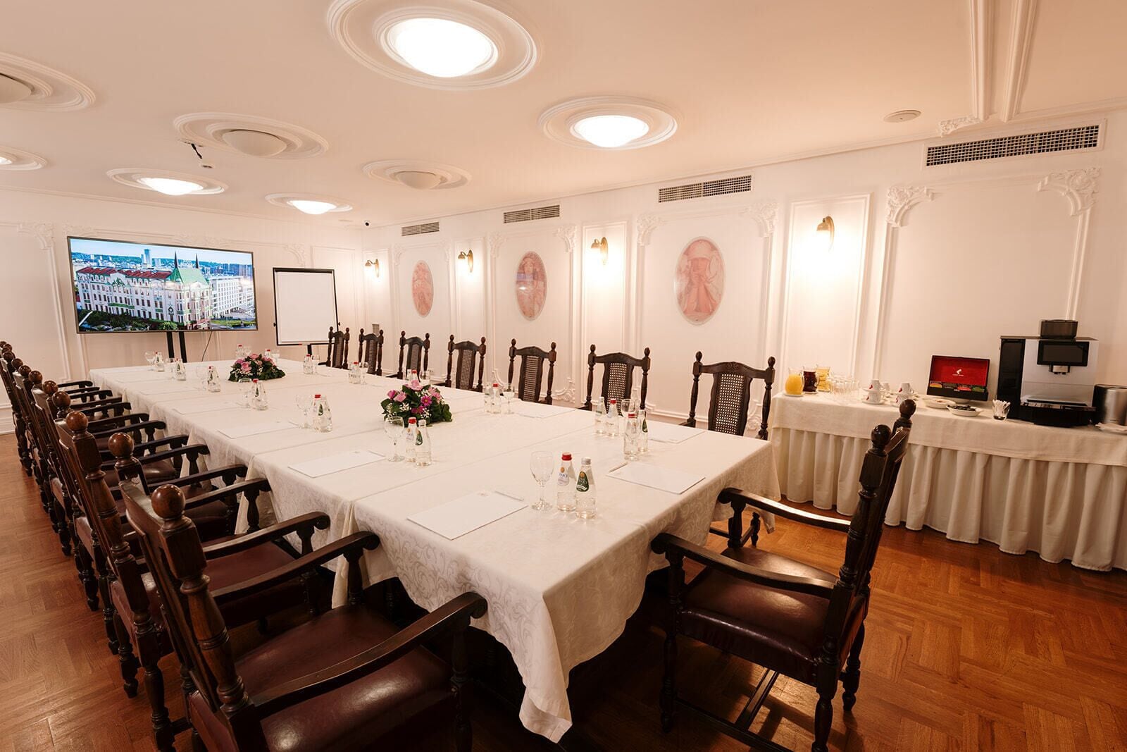 A conference room with a long table, wooden chairs, and a television screen displaying a cityscape.