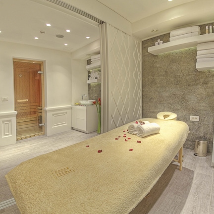 A modern spa room with a massage table, a sink, and a shower area.