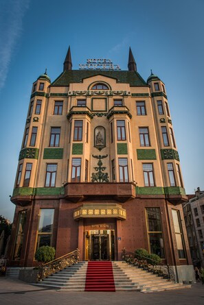 A historic building with a grand entrance, multiple windows, and a red carpet leading to the doors.