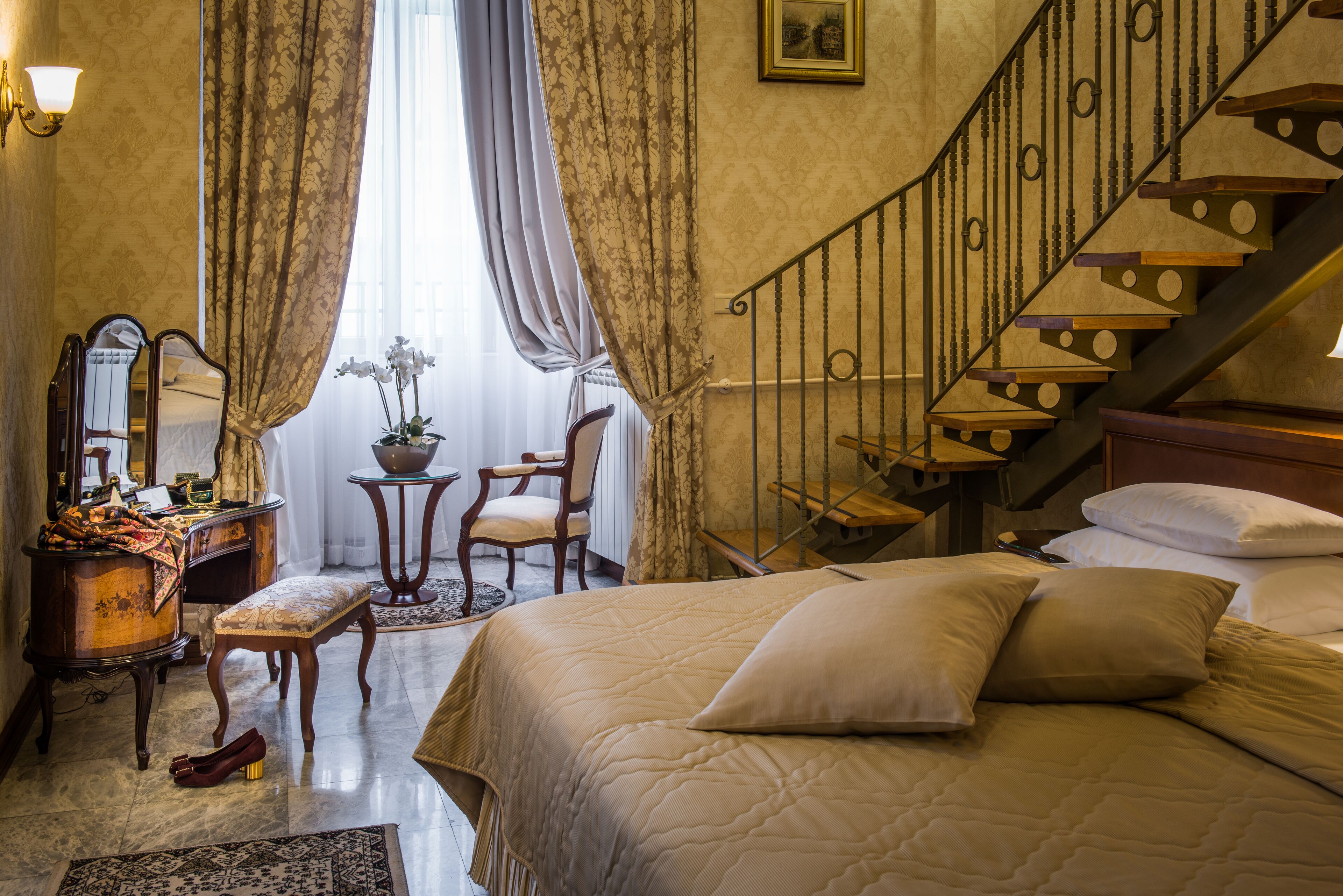 A bedroom with a bed, a chair, a desk, a mirror, a dresser, and a staircase.
