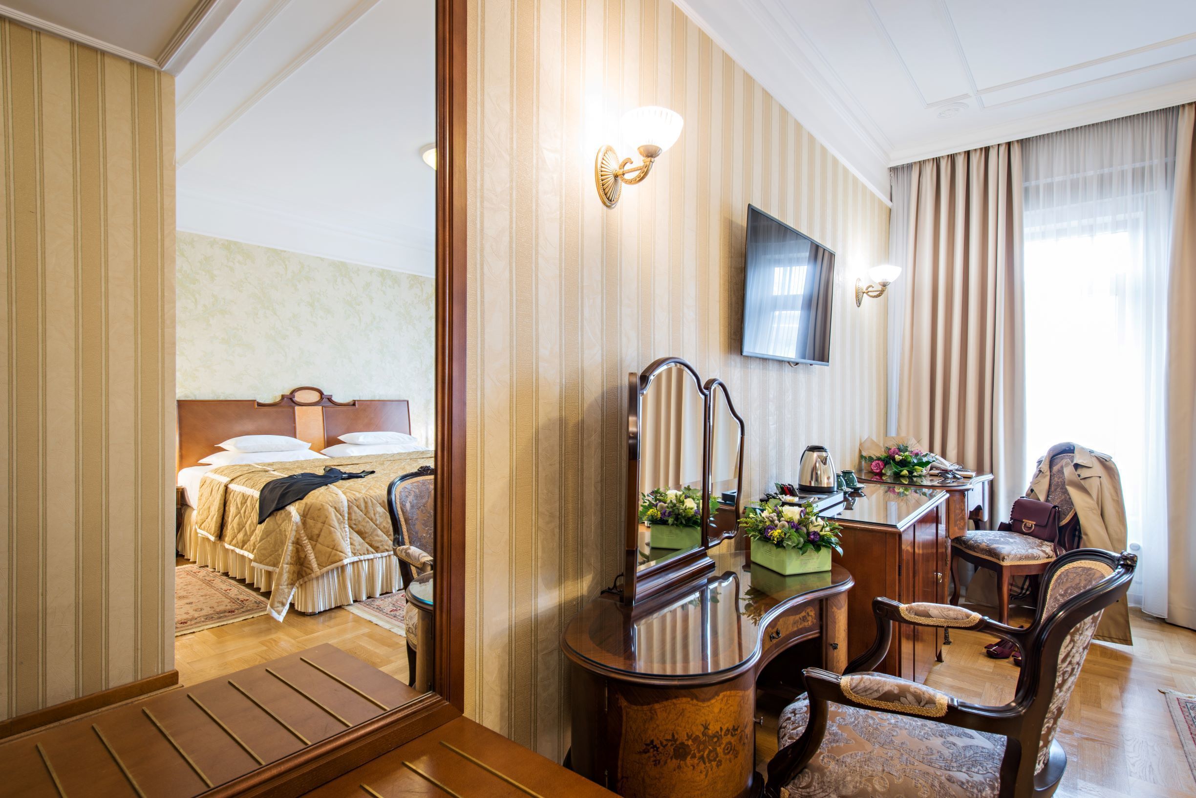 Una habitación de hotel con cama, escritorio con silla, televisión y espejo.