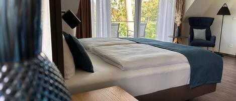 Un dormitorio con cama, mesitas de noche, una silla y vistas al exterior.