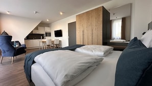 A modern hotel room with a large bed, a desk, and a kitchenette in the background. - Hotel Schöne Aussicht, Stilvoll modern, direkt am Rüstersieler Hafen (Wilhelmshaven)