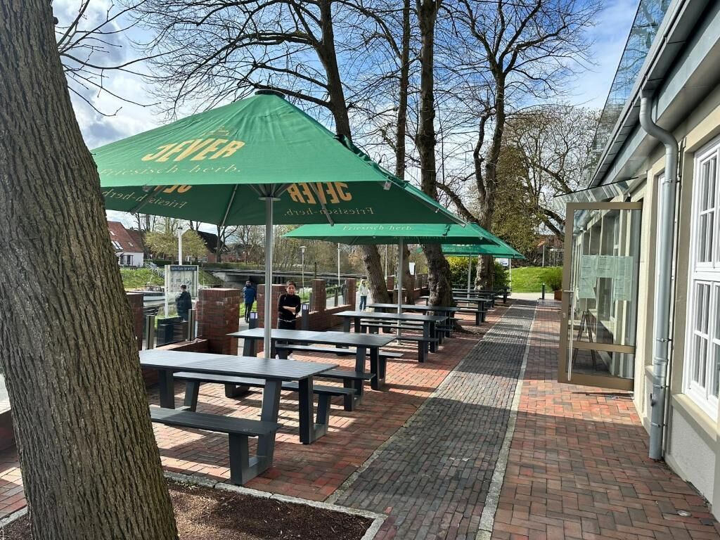 Espace extérieur aménagé avec des parasols verts, un chemin en briques et des arbres.