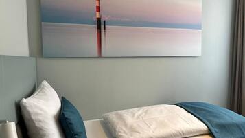 Quarto de hotel com cama, travesseiros, mesa de cabeceira, luminária e uma grande pintura de um farol na parede.