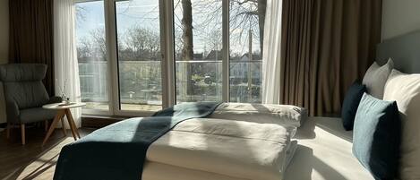 Una habitación de hotel moderna con una cama grande, una silla y vistas al exterior a través de amplios ventanales.
