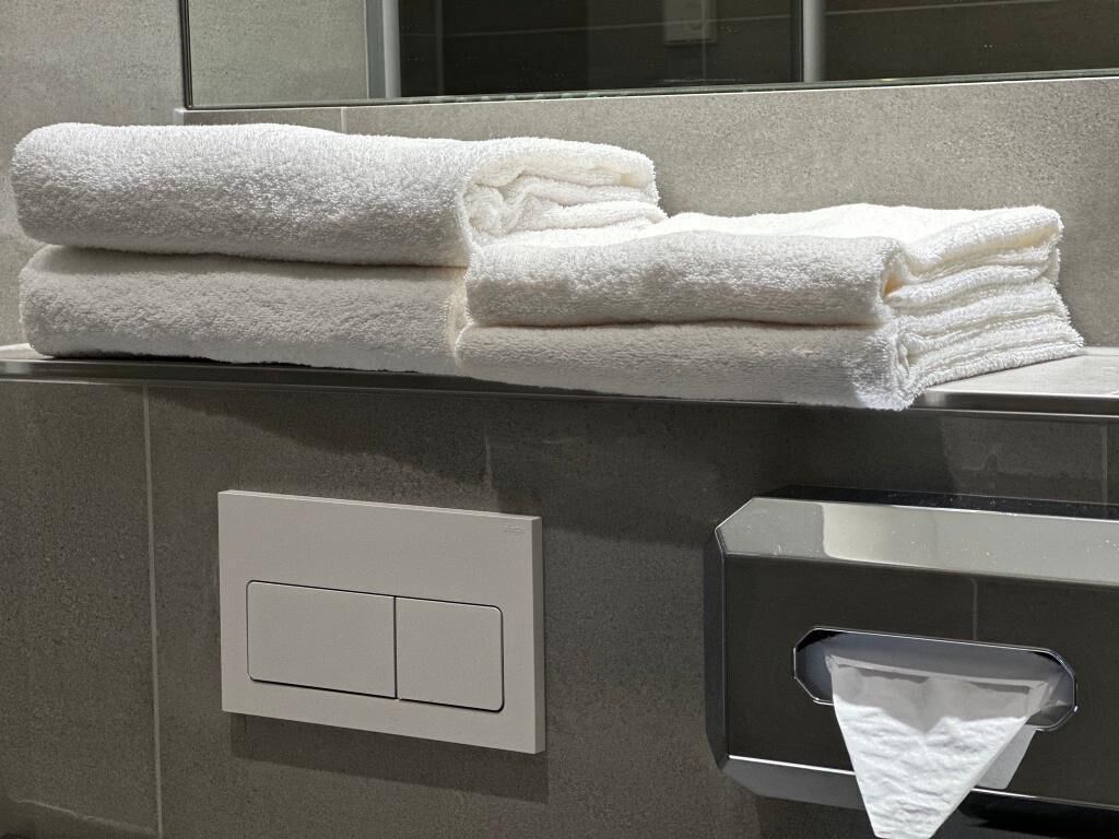 Un montón de toallas blancas sobre una encimera de baño, junto a un secador de manos.