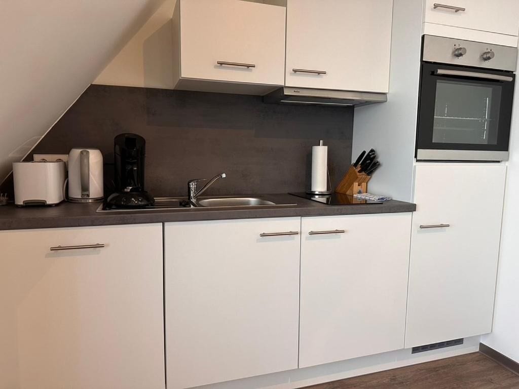 Eine moderne Küche mit weißen Schränken, einem Edelstahlbackofen, einer Kaffeemaschine und einem Messerblock.