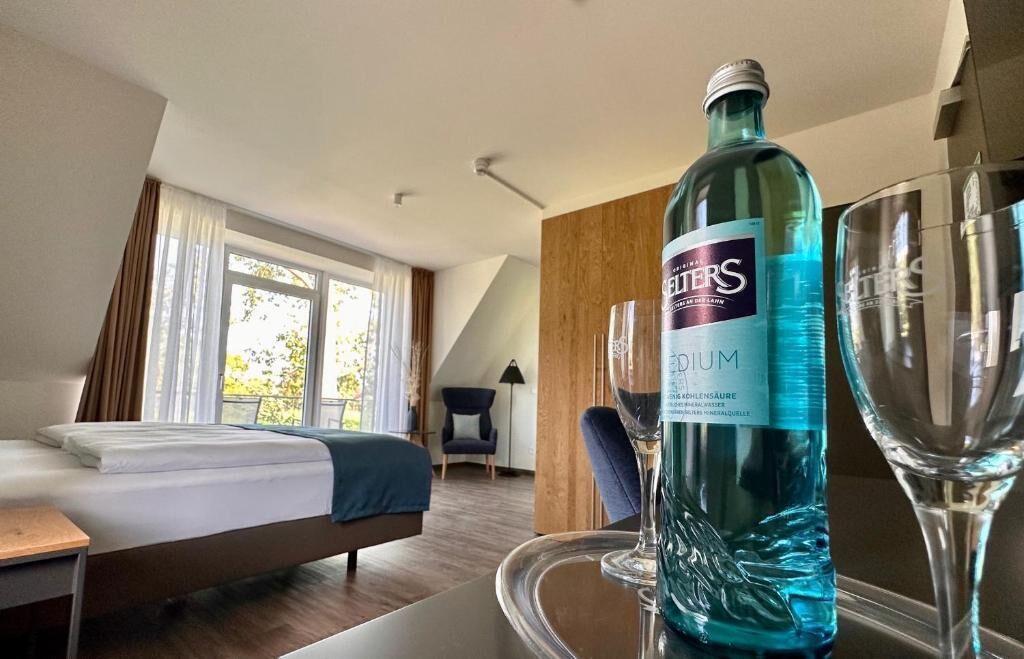 A hotel room with a bed, a table with a bottle of water, and a glass.