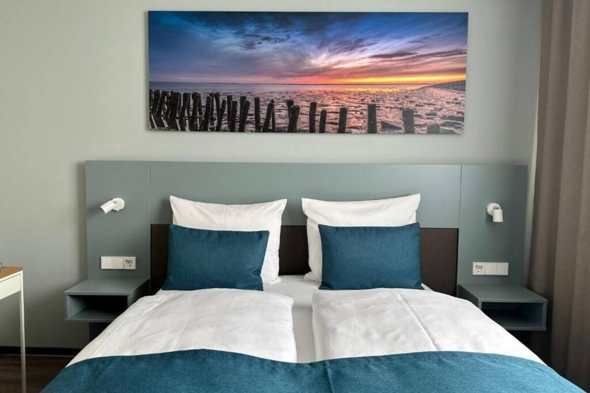 A hotel room with a bed, two nightstands, and a wall-mounted painting of a sunset over a pier.