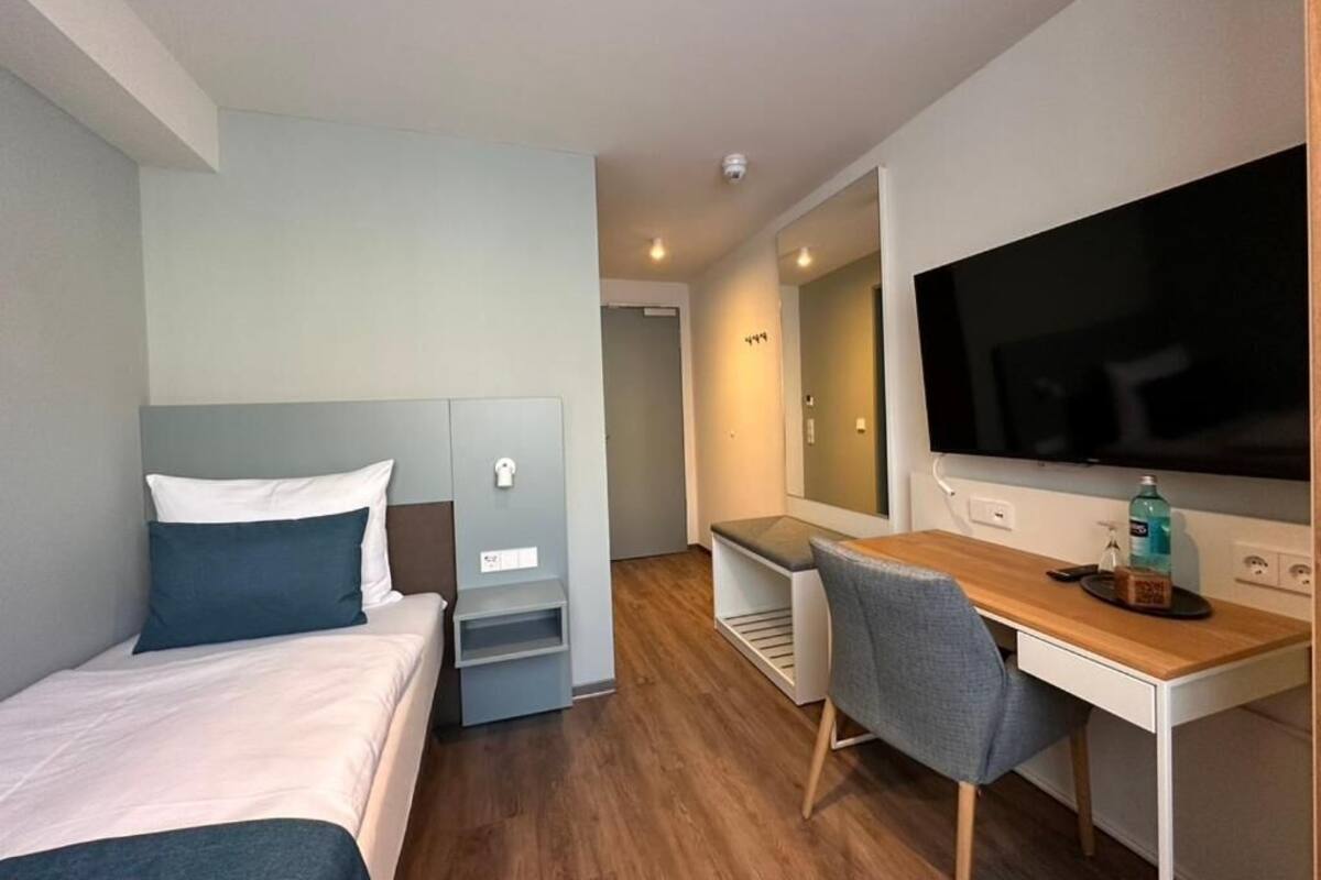 A modern hotel room with a bed, a desk, a chair, and a television.