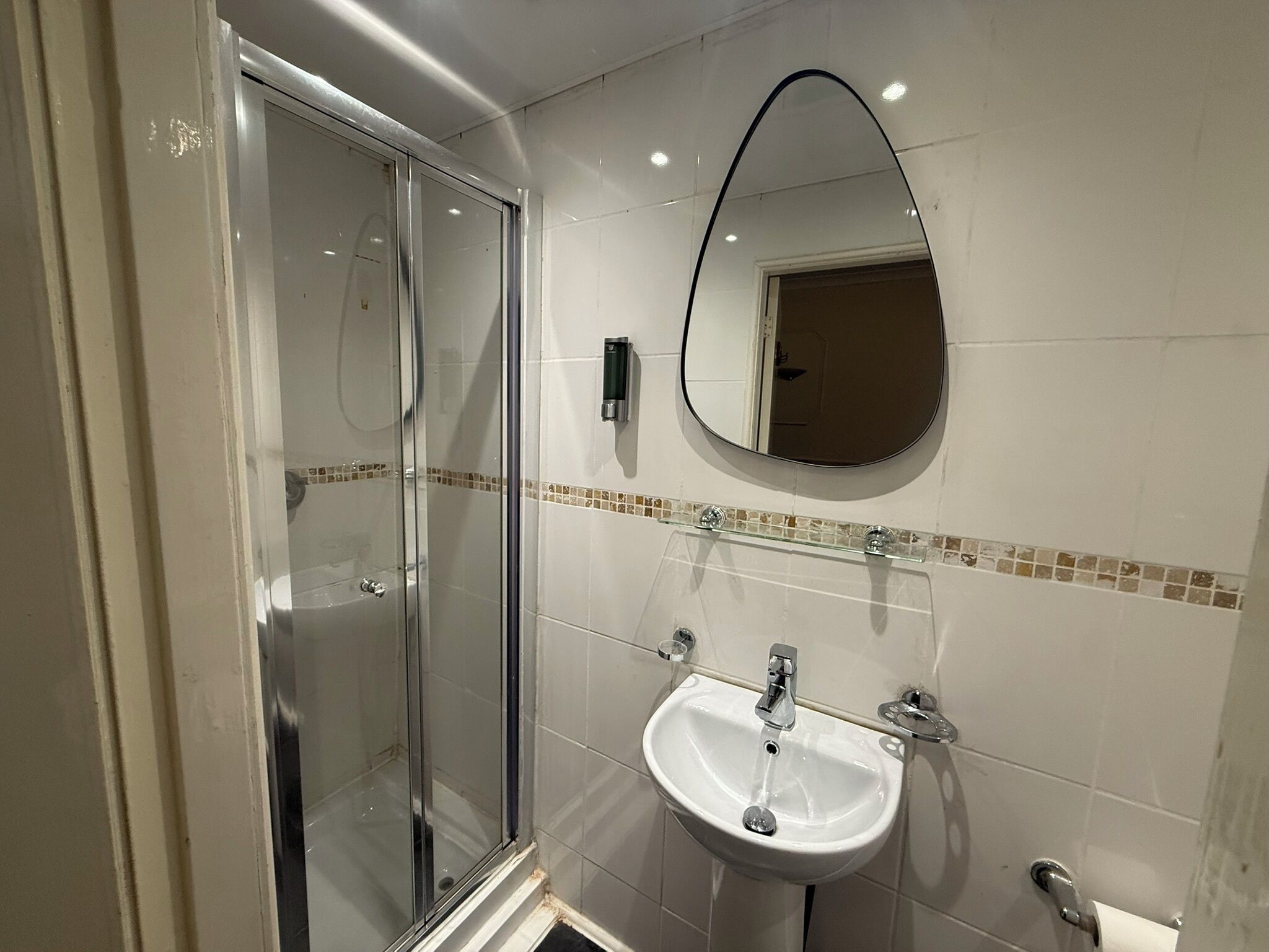 Een badkamer met een douchecabine van glas, een wit wastafelmeubel met twee kraan en een spiegel met een zwarte lijst.