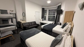 Ett hotellrum med våningssängar, en soffa, ett skrivbord, en tv och ett fönster med gardiner.