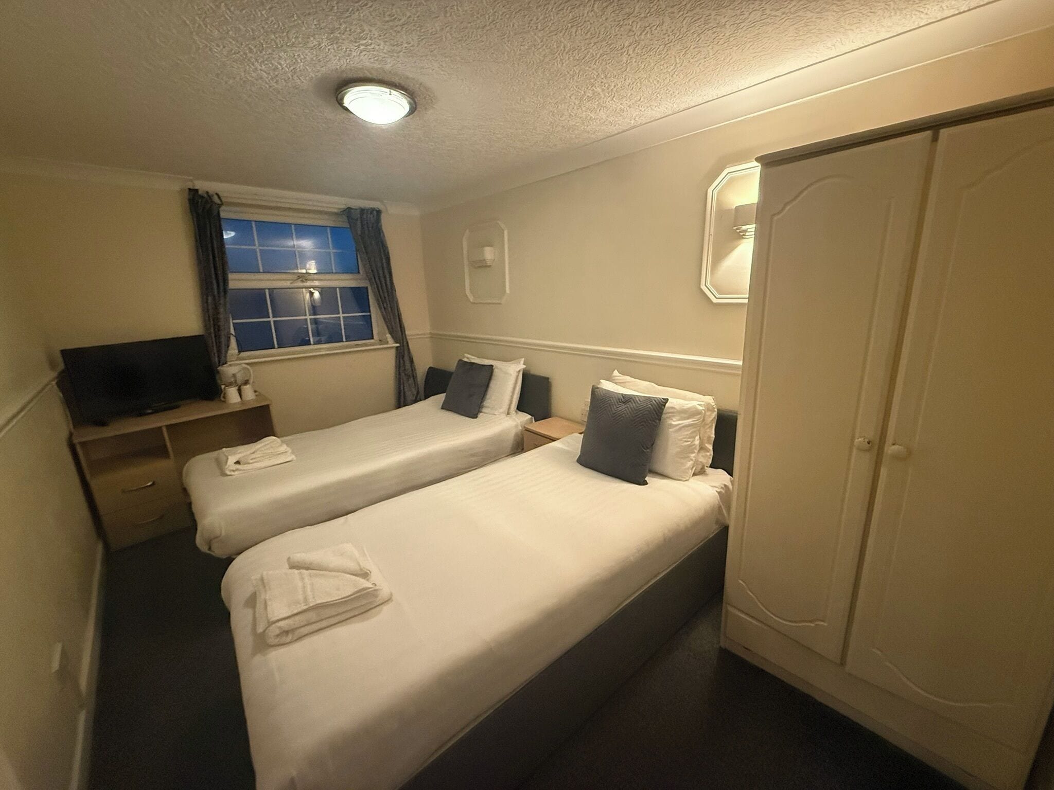 Ein Hotelzimmer mit zwei Betten, einem Fernseher, einem Kleiderschrank und einem fenster mit Vorhängen.