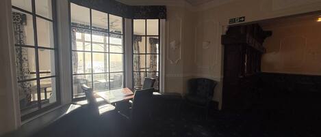 A room with large windows, a dark patterned carpet, a wooden cabinet, and a fire exit sign.