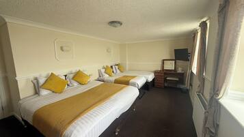 A hotel room with two beds, a desk, a chair, a radiator, and a window with curtains.