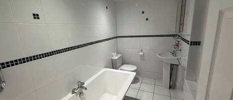 Un baño con bañera, inodoro, lavamanos y paredes con azulejos.